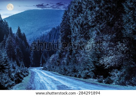 asphalt road going in mountains and passes through the conifer forest at night in full moon light