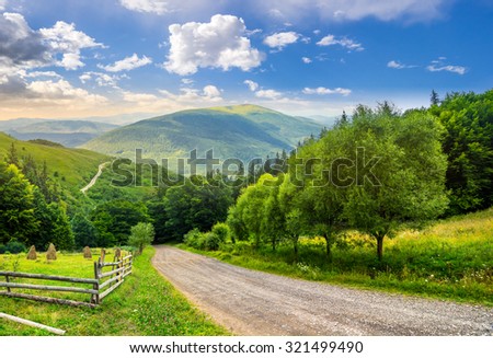 composite landscape. fence near road going down the hill through meadow and forest to the high mountains in morning light