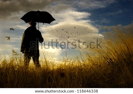Bird watching.  A composition showing a man standing in a countryside holding his umbrella. He is looking at a flock of birds passing through