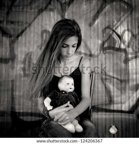 Girl with doll. A beautiful teenage girl sitting on a chair holding a doll between her arms.