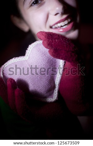 Teenage girl holding a heart. Teenage girl wearing a pair of red knitted gloves is holding and offering a pink heart