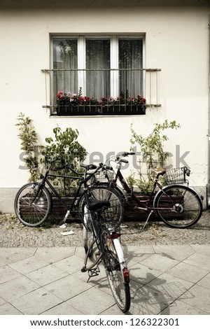 Three bikes in the pavement. Three bikes parked in a pavement under a beautiful window with flowers