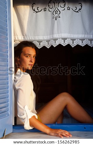 Young woman sitting in the open window of a country house watching the view