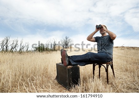 Man with binoculars in a field sitting on chair