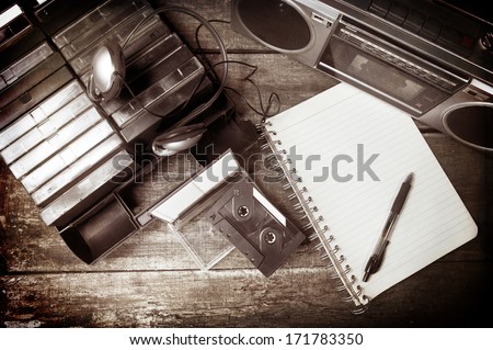 Old cassette tapes, cassette player and blank notebook on wooden surface