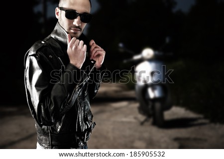 Biker in leather jacket and sunglasses posing with his scooter in an empty street
