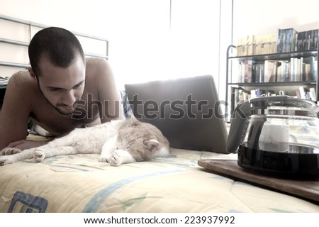 Man drinking coffee on bed while playing with his cat
