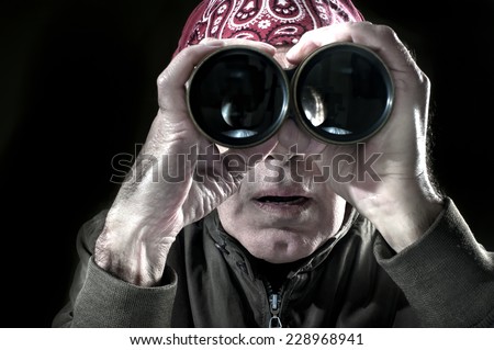 Man wearing bandana, sunglasses and jacket is looking through binoculars