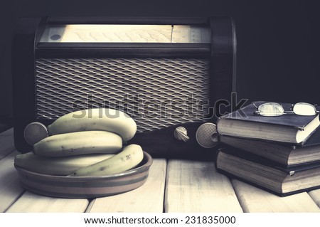 Composition with vintage items on table Vintage radio, books, glasses and bananas on wooden surface. Edited image with vintage effect