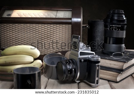 Composition with vintage items on table Vintage radio, books, glasses, old camera, whiskey and bananas on wooden surface