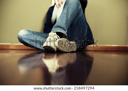 Man sitting on floor leaning on the wall. Very shallow depth of field, edited with vintage colors