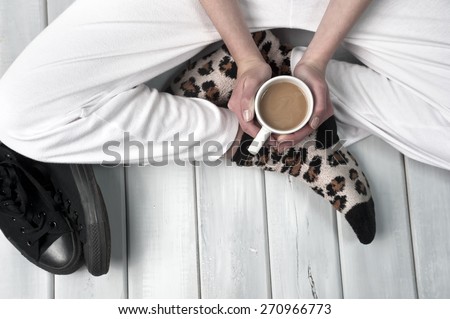 Teenage girl sitting on floor holding a coffee cup. Body part close up on wooden surface
