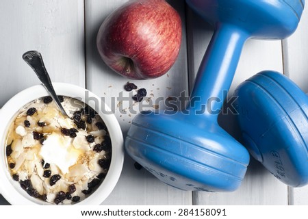 Dumbbells and red apple next to bowl with yogurt, muesli and honey on floor