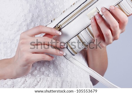 Beautiful female hands with manicure open a white handbag