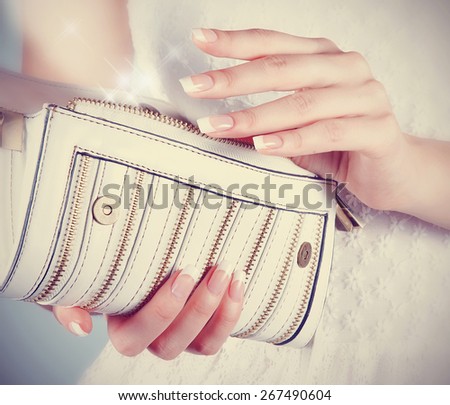 Beautiful female hands with manicure hold an open white handbag