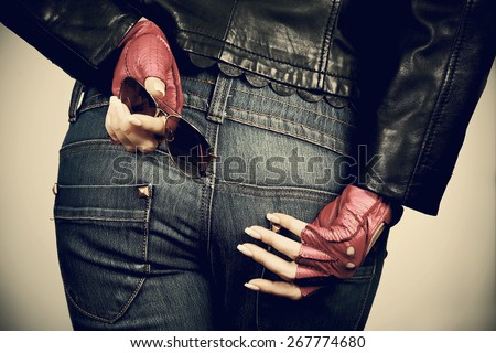 Women's hands with the sunglasses in stylish gloves back on the background of jeans