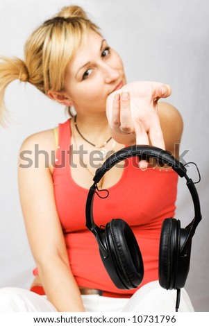 Sitting woman clothed in T-shirt and trousers holding headphones. Focus on headphones.