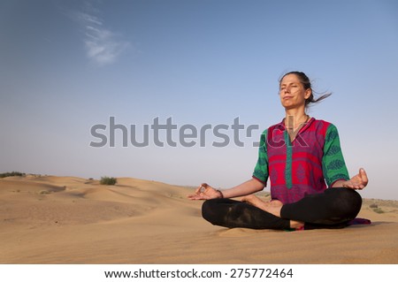 Young female practicing yoga meditation on sand dune Jaisalmer, India