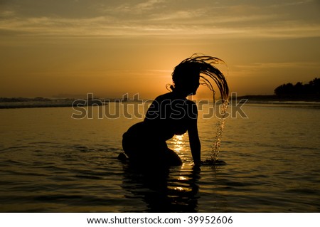 Sillouethe of young woman splashing the water with her hair on the beach during sunset