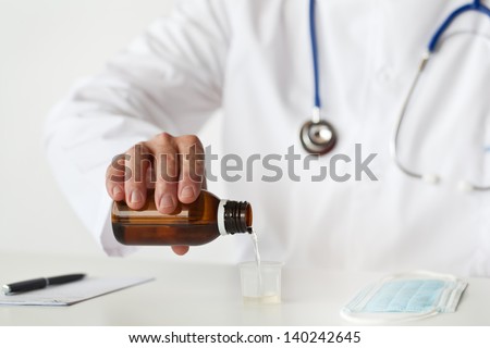 Doctor is filling a cup with cough syrup.
