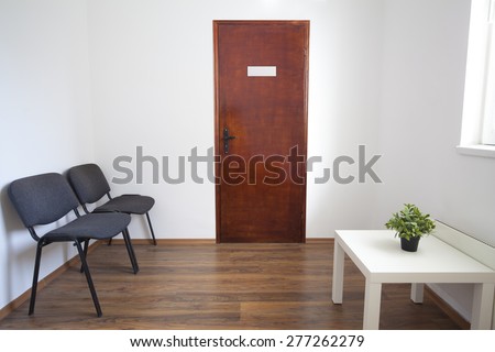 Small white waiting room without people. A doctor, dentist or other medical practitioner provides this room for the use of people who are waiting to be seen.