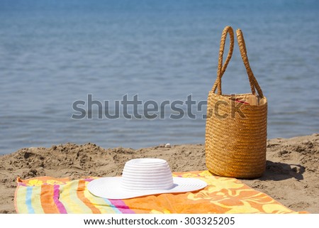 Beach accessories, bag, hat and color towel put on the sand close to the sea water.