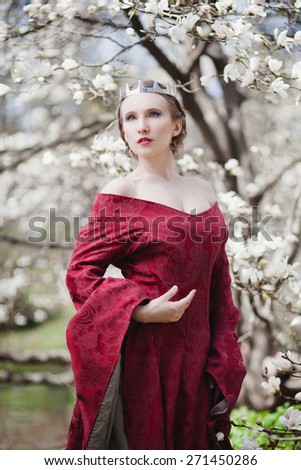 Queen in historical red dress with blossom magnolia tree