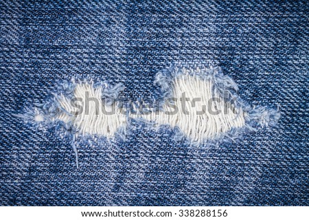 Close up texture of blue torn denim jeans with hole and threads, background
