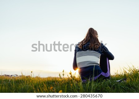 Rear view of young anonymous woman in sportswear sitting on grass in sunlight