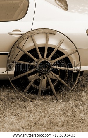 old broken wagon wheel side by new cars back sephia