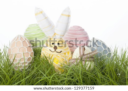 Collection of delicate pastel country Easter Eggs handcrafted with raffia, tied with a bow, covered in netting or fashioned into an adorable Easter bunny, nestling in fresh green grass
