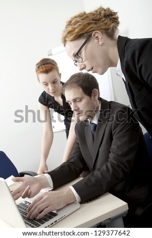 Three members of a business team brainstorming with the man gesturing towards his computer screen which they are all reading