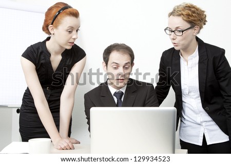 Surprised business team consisting of two women and a man gathered around a laptop computer reacting in surprise to data on the screen