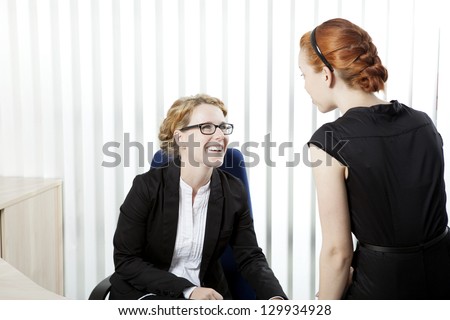 Two female business colleagues having a chat and laughing together as they share a private moment during an informal meeting in the office