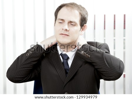 Businessman with a stiff neck or tension headache holding his hands behind his head while grimacing in pain