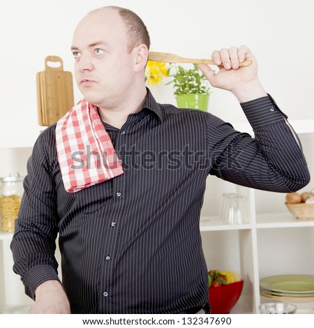 Man standing lost in thought while cooking in the kitchen absent mindedly scratching the back of his head with a wooden spoon