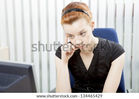 Worried despondent businesswoman sitting morosely at her desk staring at the monitor of her desktop computer