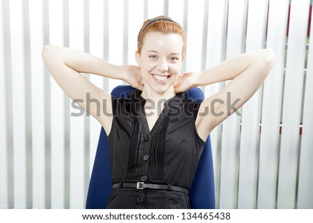 Smiling successful businesswoman leaning back in her chair with her hands behind her neck beaming at the camera