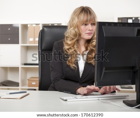 Pretty blond secretary or personal assistant working at her desk in the office typing on her desktop computer