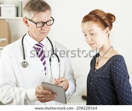 Portrait of a doctor and a young patient woman looking something on tablet pc at hospital office