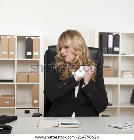Frustrated businesswoman crumpling up, a sheet of white paper as she looks to the side with a displeased expression
