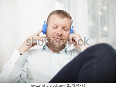 Man closing his eyes in bliss with an expression of enjoyment as he listens to music on a set of headphone while relaxing on a sofa