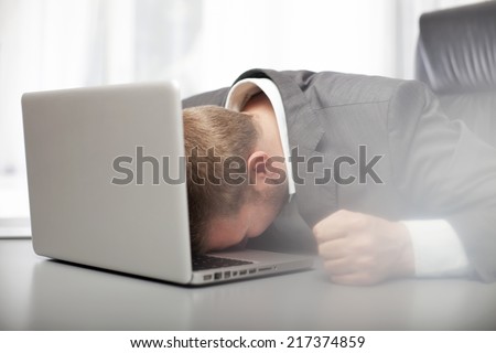 Desperate depressed businessman banging his fist on his desk and resting his head on the keyboard of his laptop computer