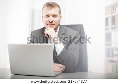 Thoughtful businessman staring at the camera resting his chin on his hand as he sits at his desk with a contemplative expression