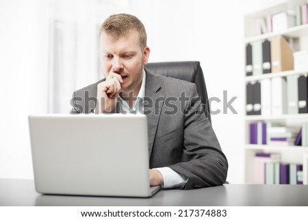 Concerned businessman working at his desk in the office staring at the screen of his laptop computer with a worried expression
