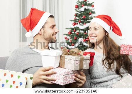 happy young couple giving christmas presents in front of christmas tree