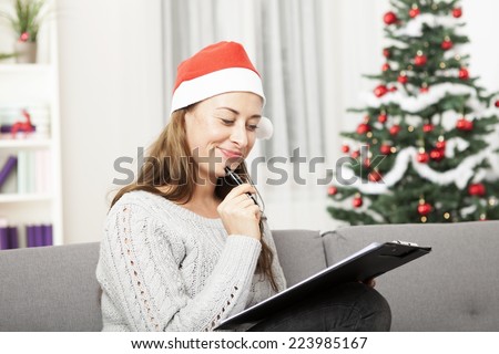young happy woman think about christmas with list on sofa in front of christmas tree.
