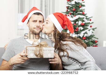 man is skeptical about christmas gift  while his girlfriend give him a kiss