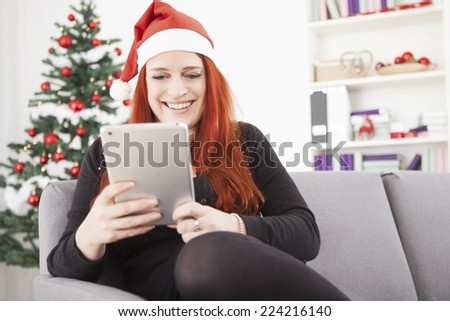 happy young red haired girl with santa hat is shopping something for christmas on the tablet