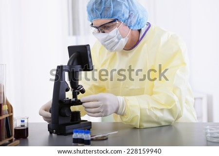 portrait of scientist or doctor in protective gear working with microscope and blood, in lab or hospital